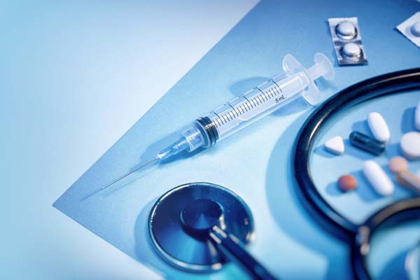 photo showing a syringe, assorted medications in pill form, and a stethoscope on a blue background